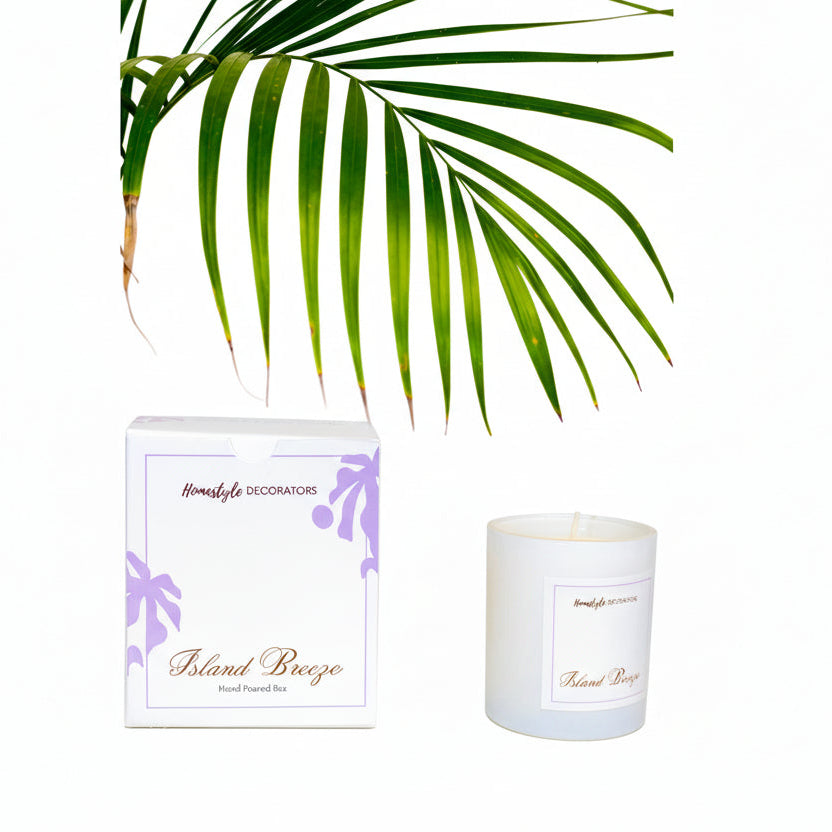 Candle labeled 'Island Breeze' by Homestyle Decorators with a palm leaf in the background.