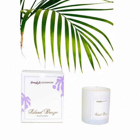 Candle labeled 'Island Breeze' by Homestyle Decorators with a palm leaf in the background.
