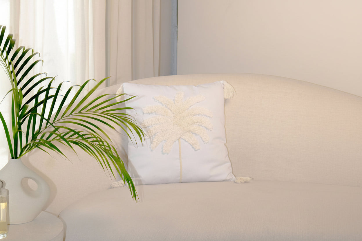 Decorative pillow with palm tree design on a light-colored sofa next to a plant.